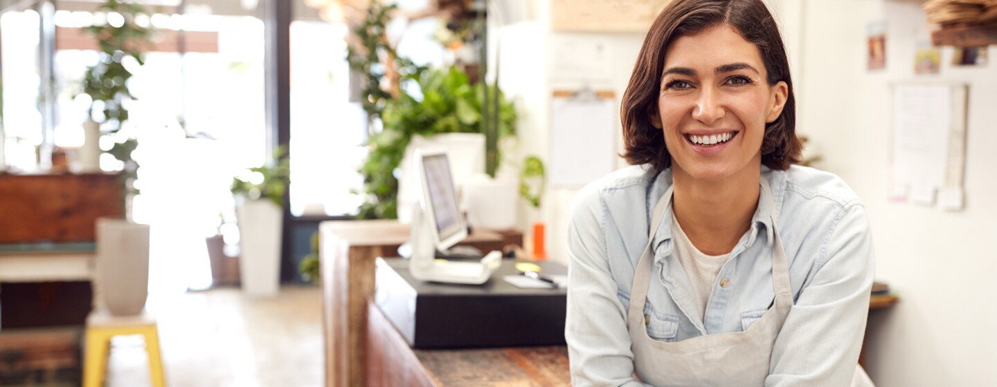 A woman working in a small business leans toward the camera.