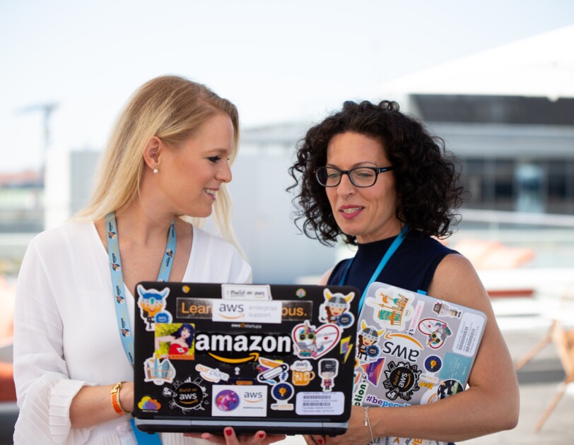 Zwei Frauen halten einen Laptop in den Händen auf dem Amazon steht. Sie sprechen miteinander.