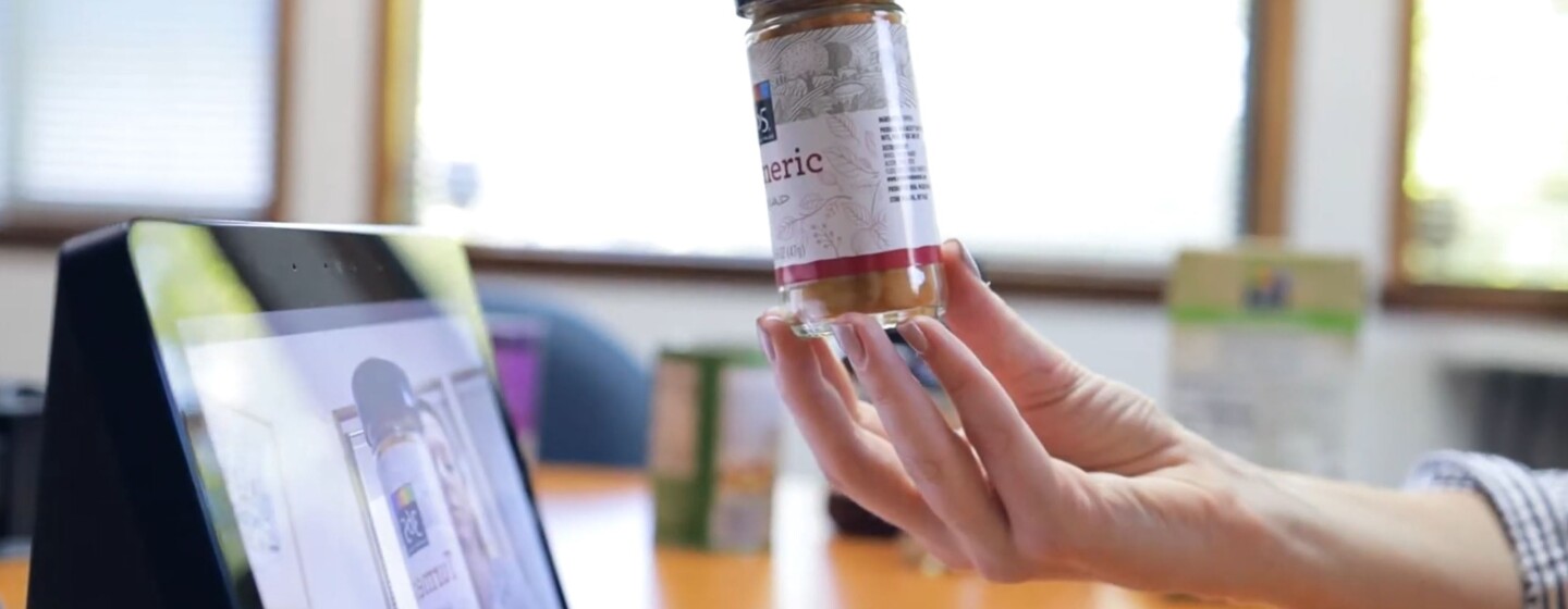 A hand holds a spice jar of Turmeric in front of an Echo Show to identify the product.