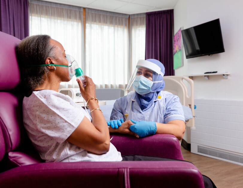 NHS carer in PPE and patient sitting in chair with oxygen mask