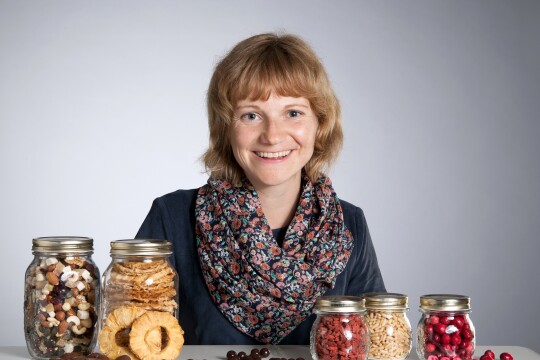 Frau mit kurzen Haaren sitzt vor einem Tisch, auf dem Einmachgläser mit getrocketen Früchten stehen