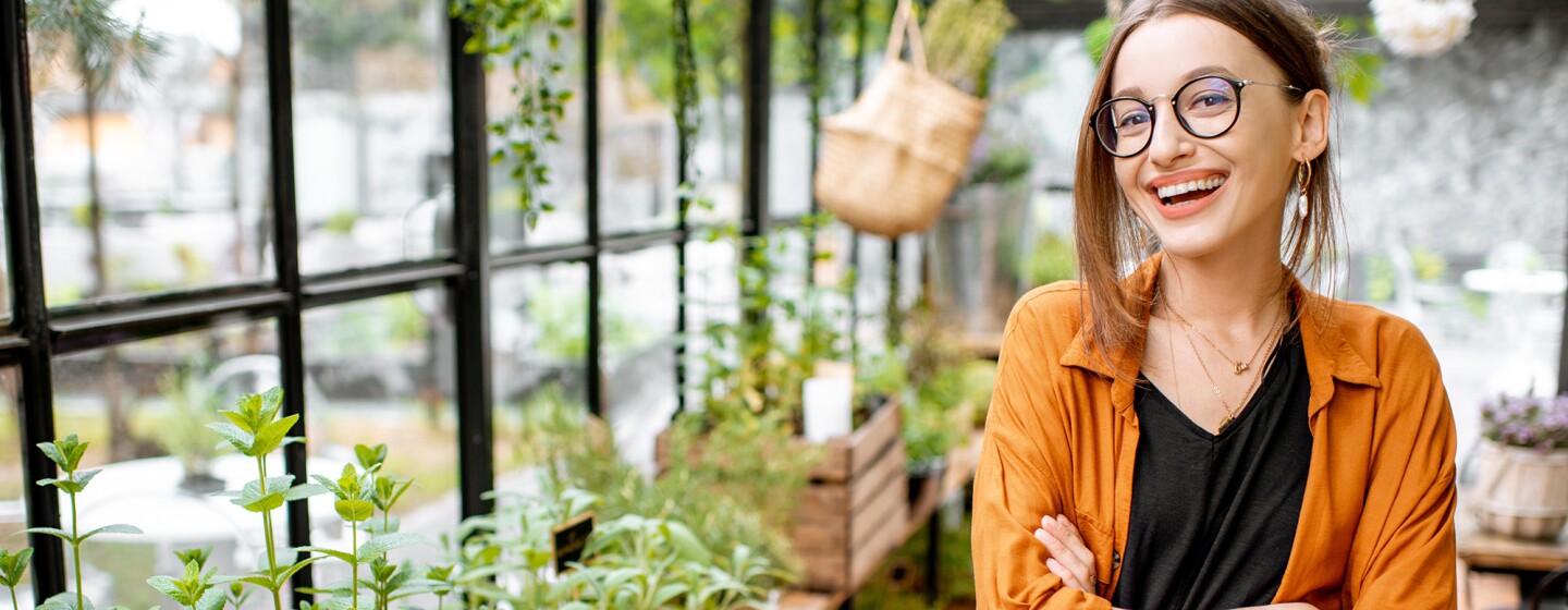 A woman smiles from inside a green house, her arms crossed.