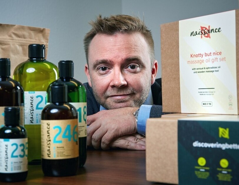 Man dressed in a suit, positioned behind bottles and cardboard boxes