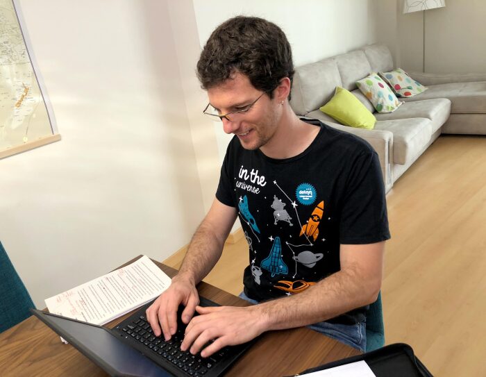 Cristian Perfumo, el escritor de la Patagonia, está sentado en una mesa de comedor y trabajando en su ordenador. Viste una camiseta deportiva y en la mesa tiene unas hojas de papel con correcciones en color rojo.