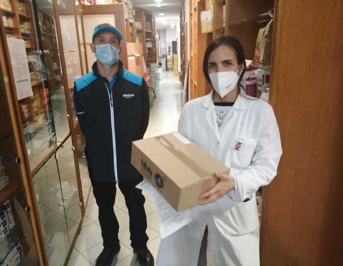 Un autista Amazon consegna un pacco di medicinali ad una farmacista, che indossa un camice bianco.