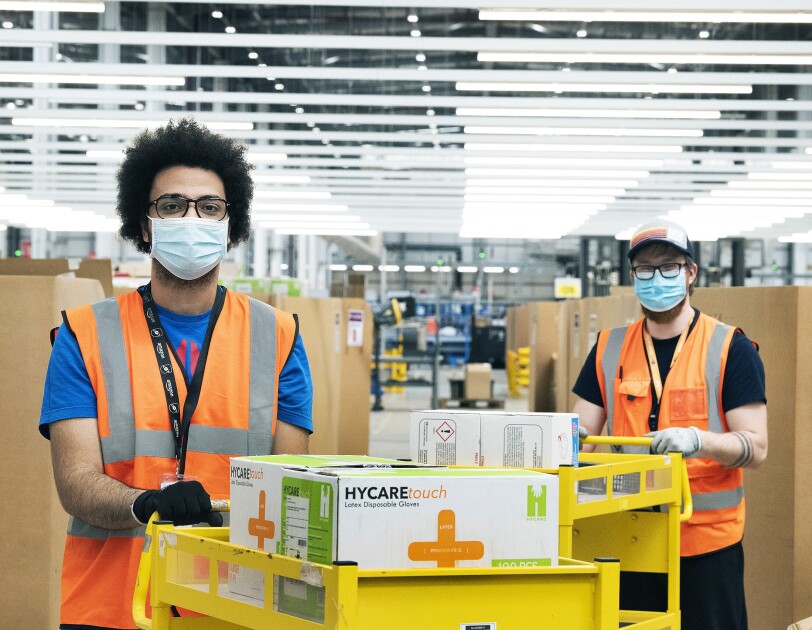 Amazon employees in a fulfilment centre packing medical supplies ready for the government into boxes. They are wearing hi-vis jackets and face masks.