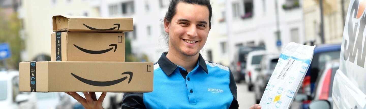 Ein junger Amazon Fahrer im blauen Amazon-Shirt stellt Pakete zu.