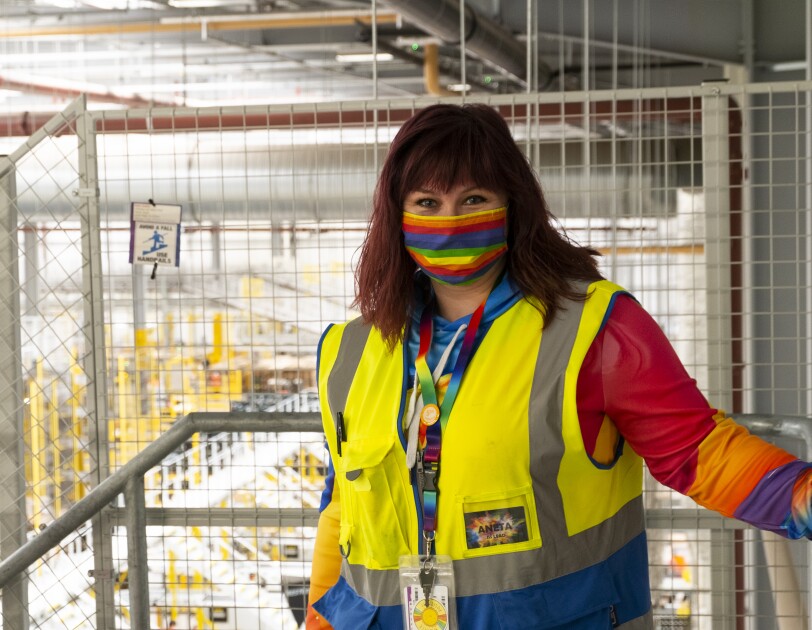 Amazon FC Lead Aneta Bachledova-Pateman wearing a yellow vest and a rainbow face mask, inside an Amazon site