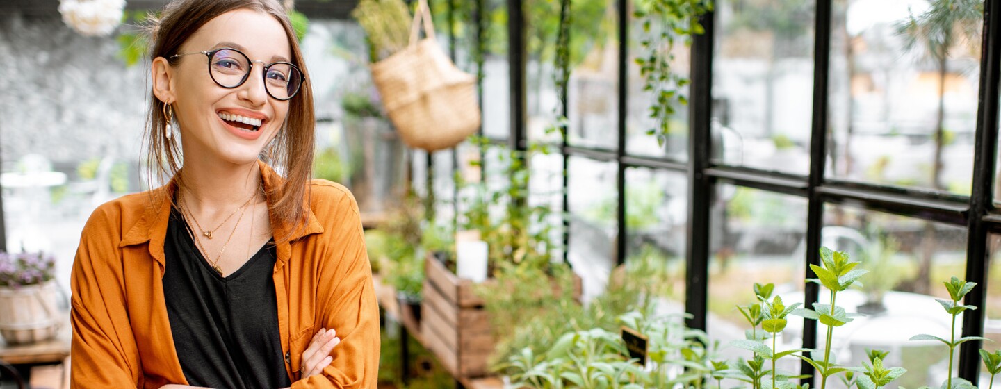 A woman smiles from inside a green house, her arms crossed.