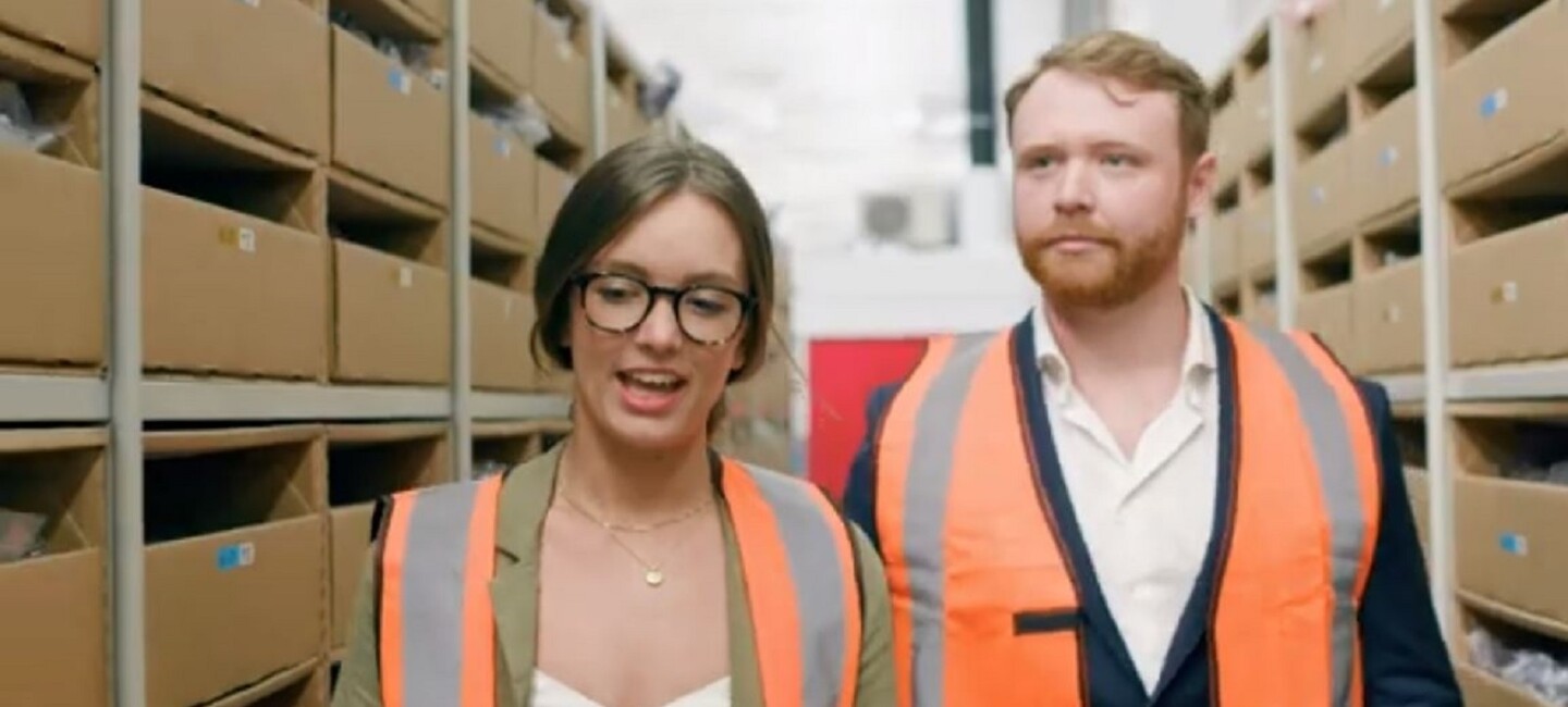 Woman and a man in high-vis walking through a warehouse eisle