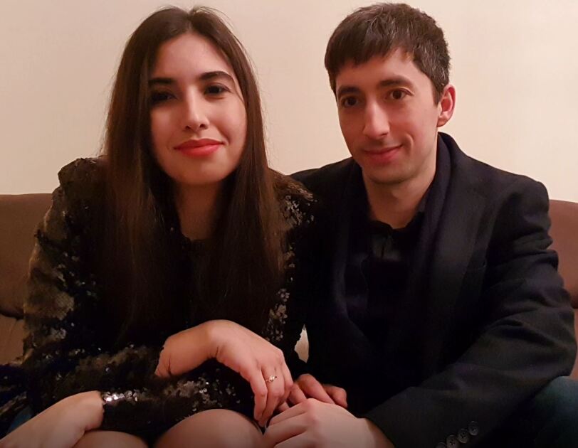 Une femme brune et un homme brune sont assis ensemble sur un canap&eacute;, de l&eacute;gers sourires sur leurs visages. 