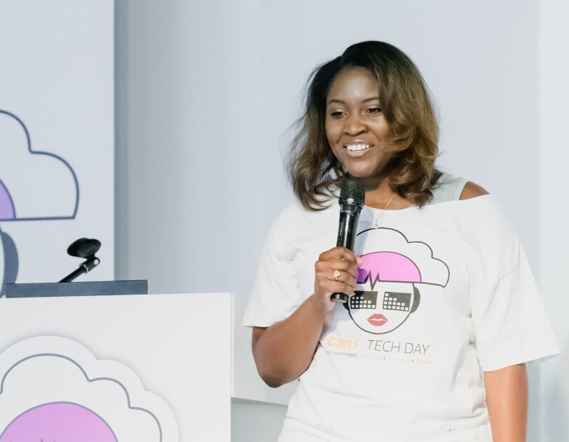 Cornelia Robinson, Global Leader of AWS InCommunity holding a microphone and wearing a Girls' Tech Day T-shirt speaks at an AWS InCommunity event