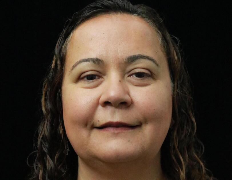 Dilek Hakkani-Tür, a senior principal scientist in the Alexa AI group smiles at the camera. She wears a gray button down shirt and her brown hair is pulled back in a low pony tail.