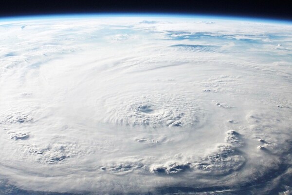 Foto de la tierra desde el espacio. Se ven nubes de color blanco y azul. También se ve una parte de cielo oscuro. 