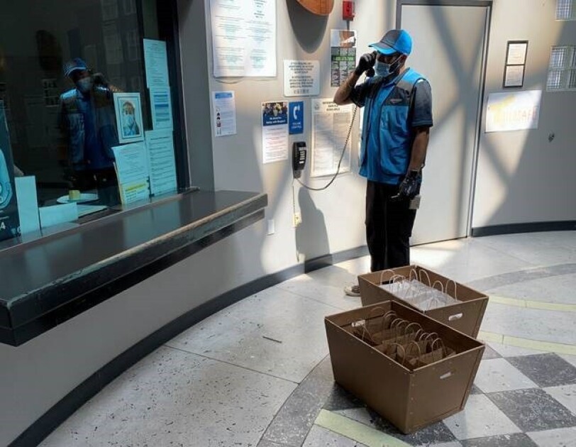 A delivery driver tasks on a landline phone while standing near two boxes filled with individual bags.