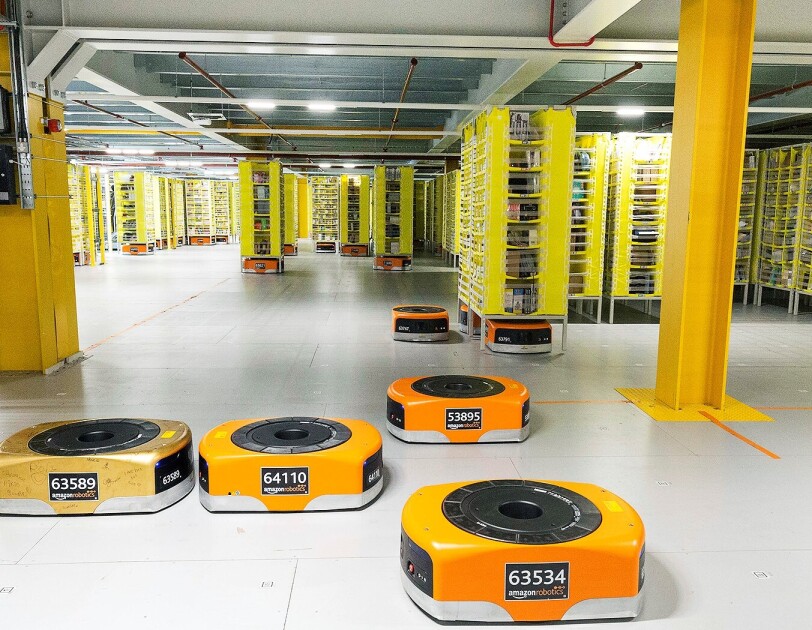 Several orange robots are pictured in a Fulfillment Center as they help move products across the floor.