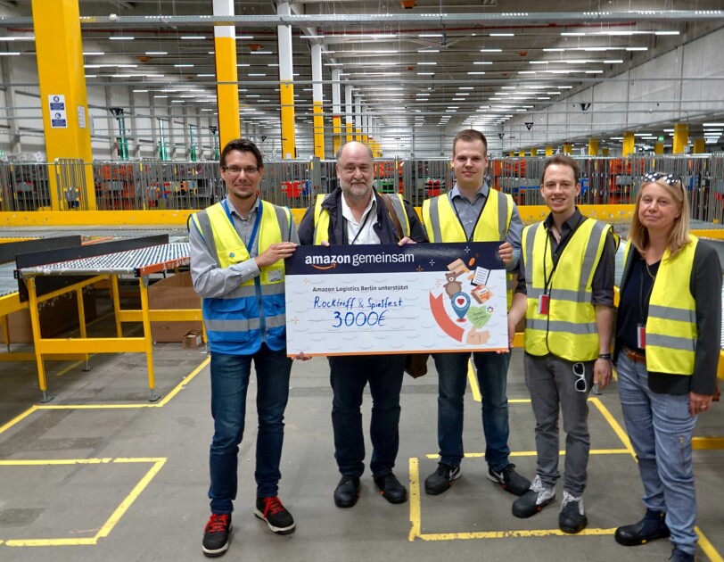Fünf Personen stehen im Verteilzentrum bei Amazon und halten einen Spendenscheck