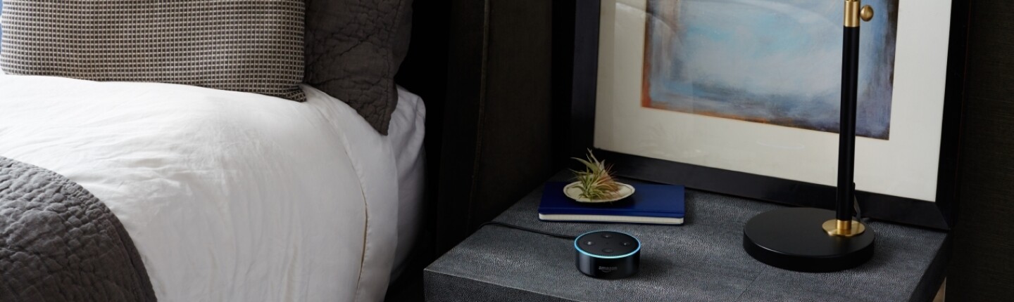 A black Amazon Echo Dot on a black nightstand.