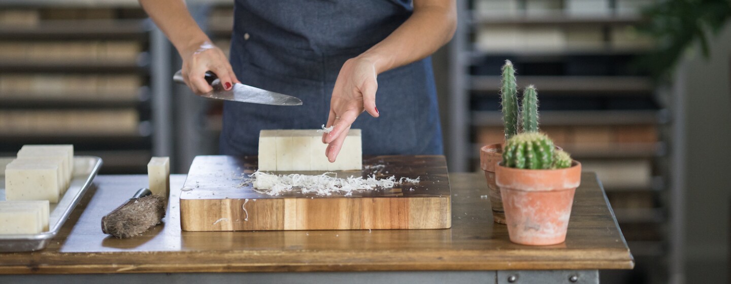 An employee at Little Flower Soap Company cuts a block of soap by hand, to create bars of soap to be packaged and shipped to customers.