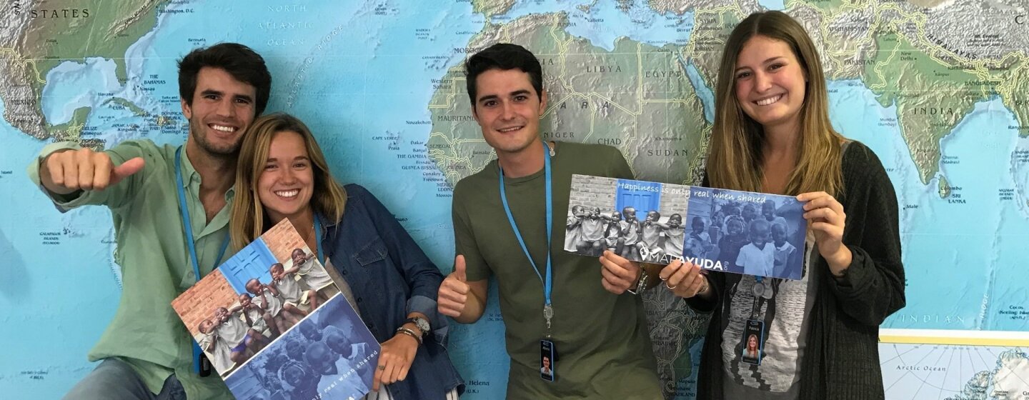 Delante del mapa del mundo, cuatro amazonians, se muestran en actitud informal: dos mujeres con folletos de la iniciativa solidaria para la que están trabajando y los dos hombres haciendo la señal de OK a cámara.