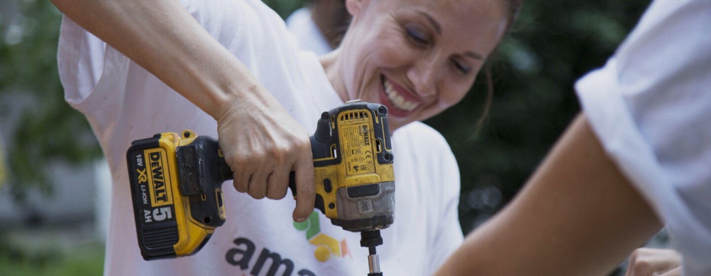 Volontaria di Amazon sorride in primo piano mentre regge un trapano durante i lavori alla Scuola Media Leonardo da Vinci di Affori, nella periferia di Milano.