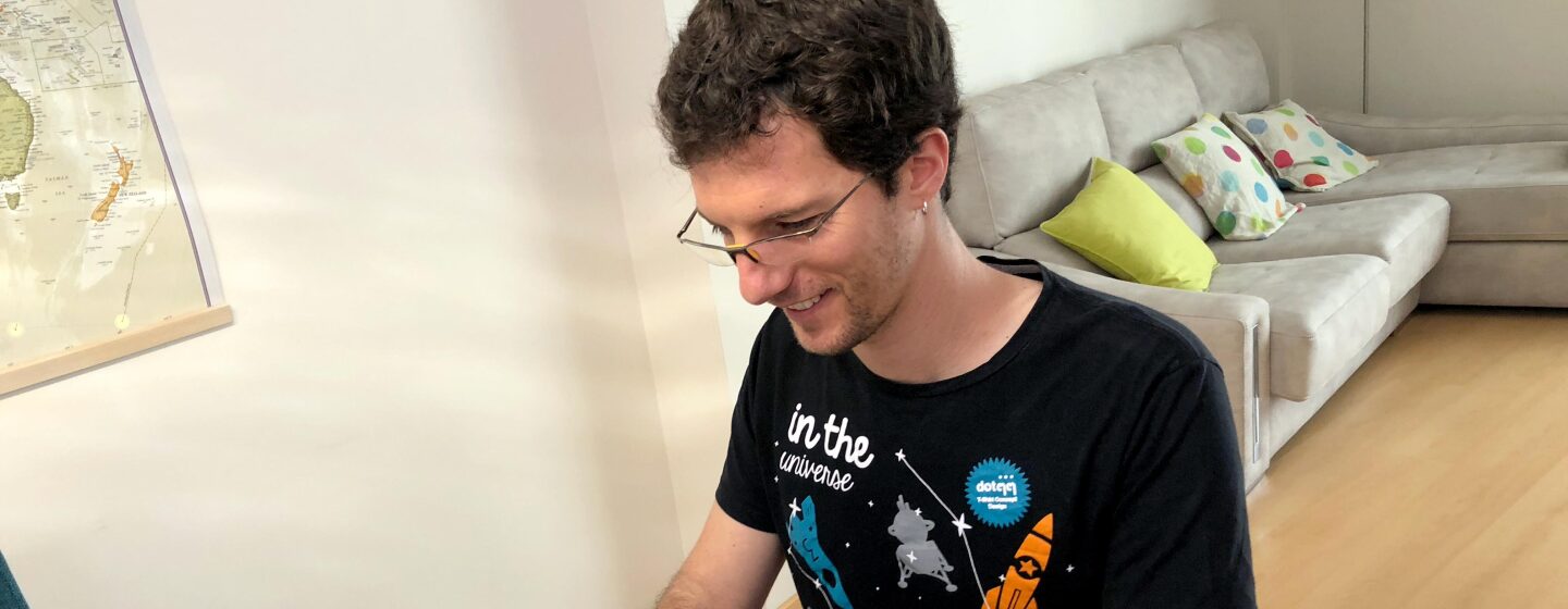 Cristian Perfumo, el escritor de la Patagonia, está sentado en una mesa de comedor y trabajando en su ordenador. Viste una camiseta deportiva y en la mesa tiene unas hojas de papel con correcciones en color rojo.