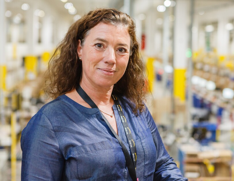 Eine braunhaarige Frau in blauer Bluse in einem Logistikzentrum.