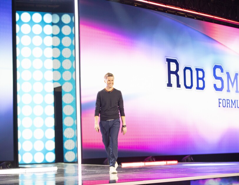 Rob Smedley, Formula 1 engineer standing on stage at the AWS re:Invent 2019 event. He is in front of a large screen with his name on it.