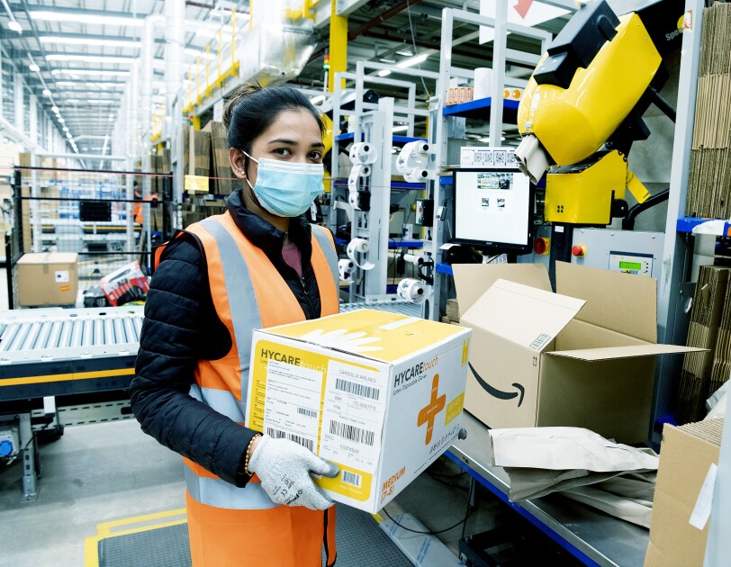 An Amazon fulfilment centre employee packing boxes with medical supplies in the Coalville Fulfilment centre to provide supplies to the relevant government centres. She is wearing protective gloves and a face mask.