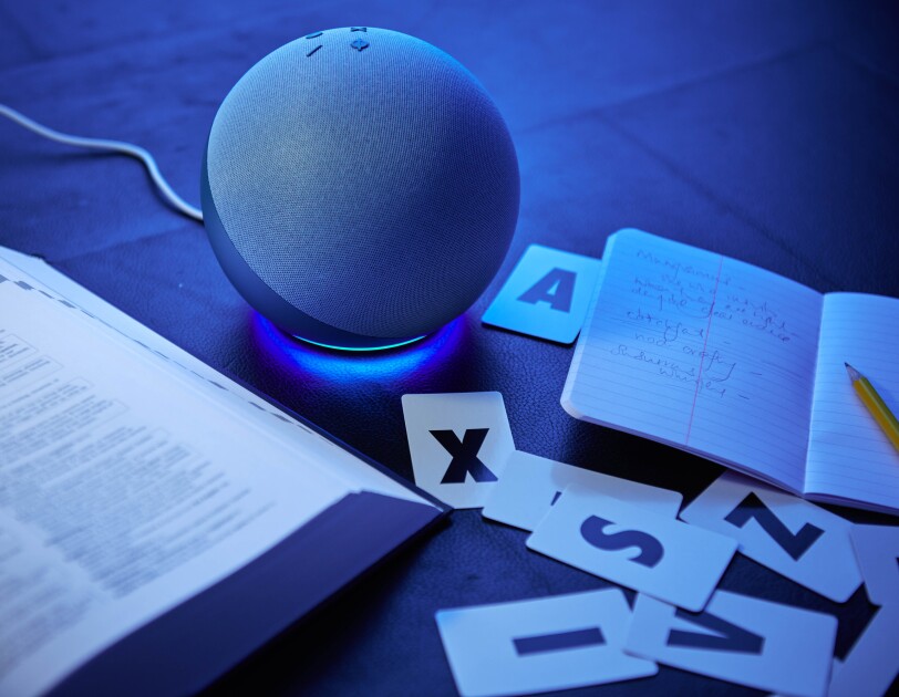 An Amazon Echo on a library table next to a dictionary and letter cards.
