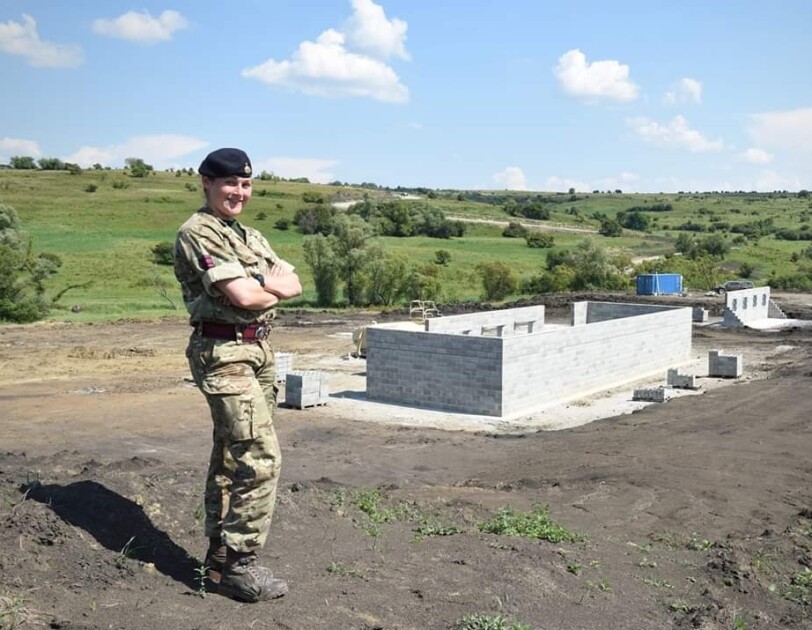 Reservist, Sophie Martin, standing cross-armed and dressed in her Army uniform with an outdoor military facility in the background.