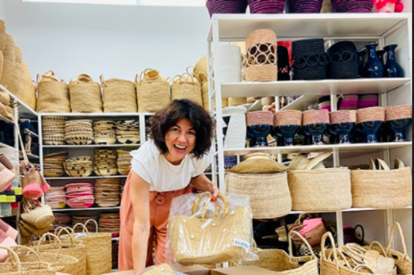 A smiling woman with woven baskets places them into a cardboard box.