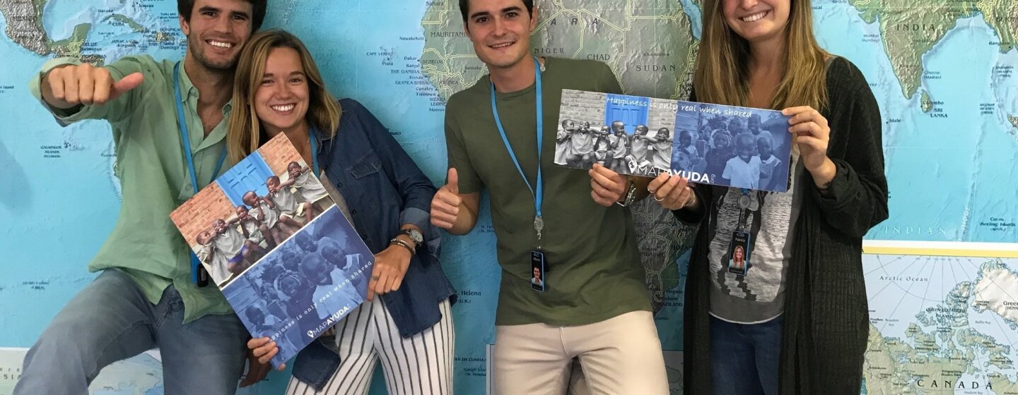 Delante del mapa del mundo, cuatro amazonians, se muestran en actitud informal: dos mujeres con folletos de la iniciativa solidaria para la que están trabajando y los dos hombres haciendo la señal de OK a cámara.