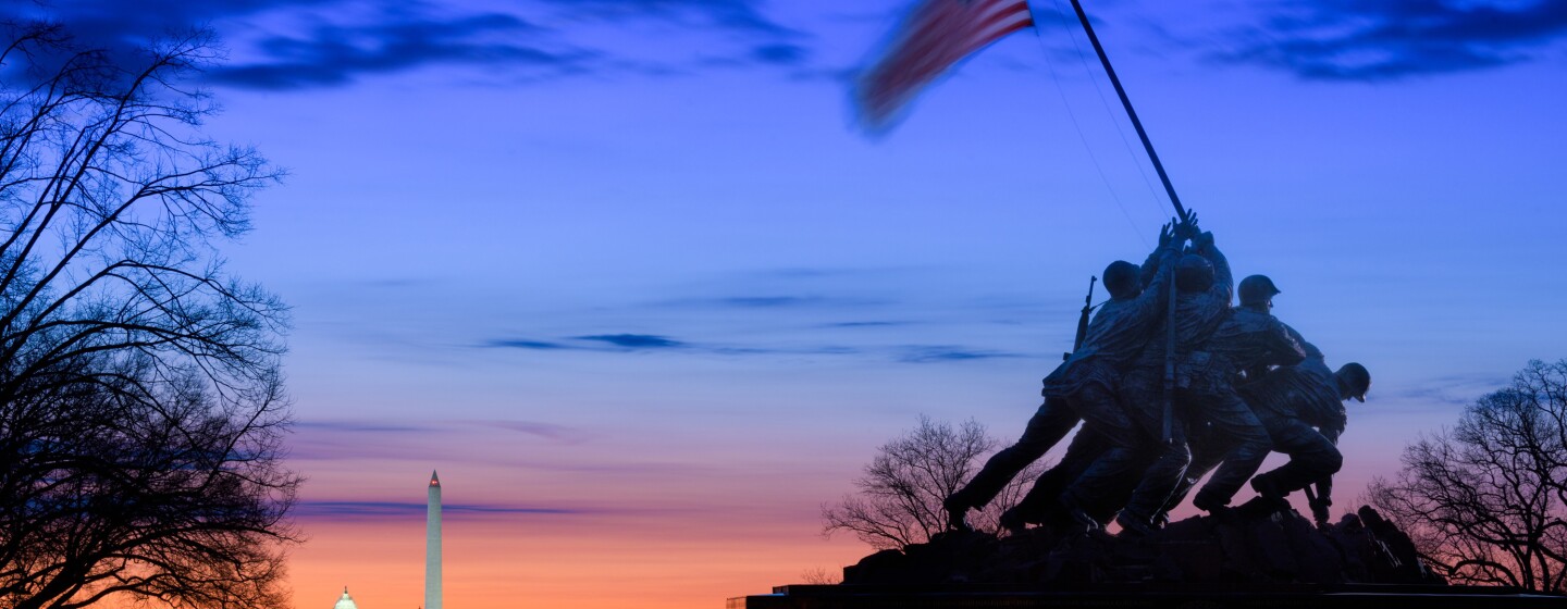US Marine Corps War Memorial in front of a sunset with the Lincoln Memorial, Washington Monument, and US Capitol dome receding toward the horizon