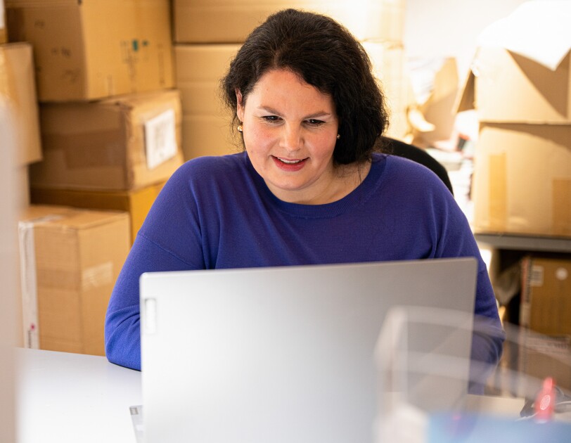 Eine Frau in einem blauen Pullover schaut in einen grauen Laptop.