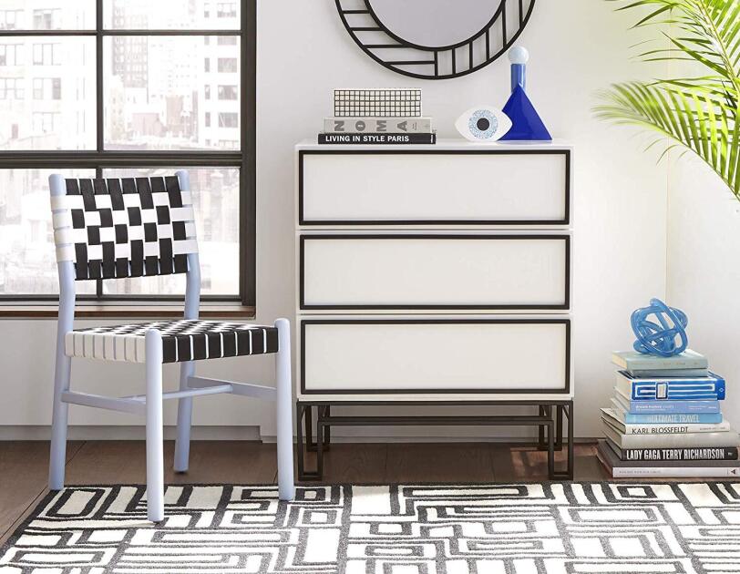 Dining chair sits next to a modern dresser topped with three books, and decor items. A pattern-framed mirror hangs on the wall, next to a tall fern.
