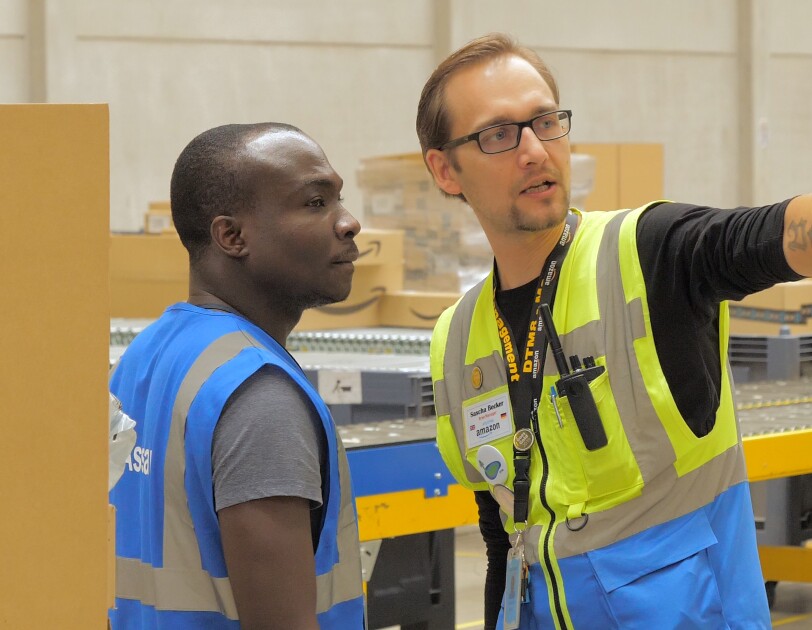 Sascha (rechts) im Gespräch mit einem Mitarbeiter. Beide tragen Sicherheitswesten.