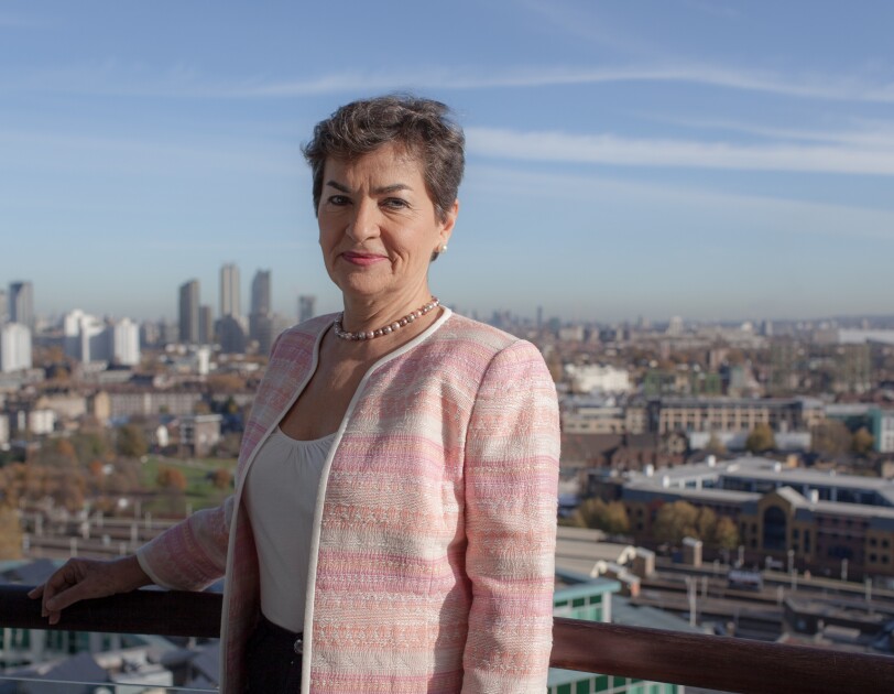 Christiana Figueres standing on a balcony overlooking a city skyline.