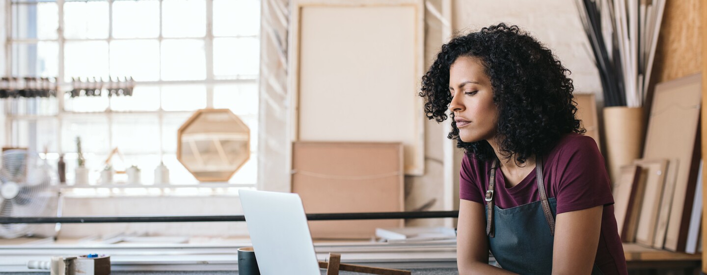 A woman entrepreneur sits at a workbench, while working on her computer.