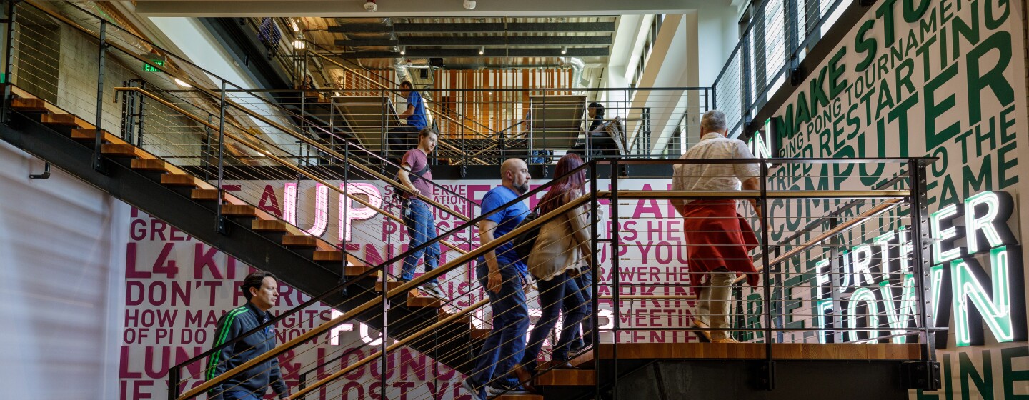 Amazon employees climb a set of stairs that are decorated with inspirational slogans, like "try something new".