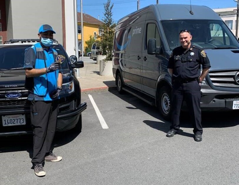 A police officer and a delivery driver stand near a delivery van.
