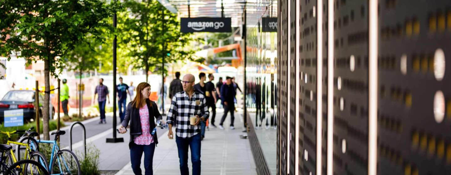 Amazon employees walk on the sidewalk past Amazon Go flagship store in Seattle, Washington