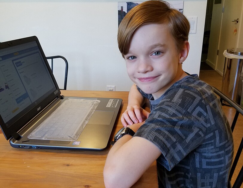 An elementary age student sits with their laptop computer in their home