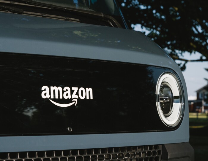 Primo piano del fronte del furgone Rivian, con il logo Amazon al centro e un fanale del furgone sulla destra
