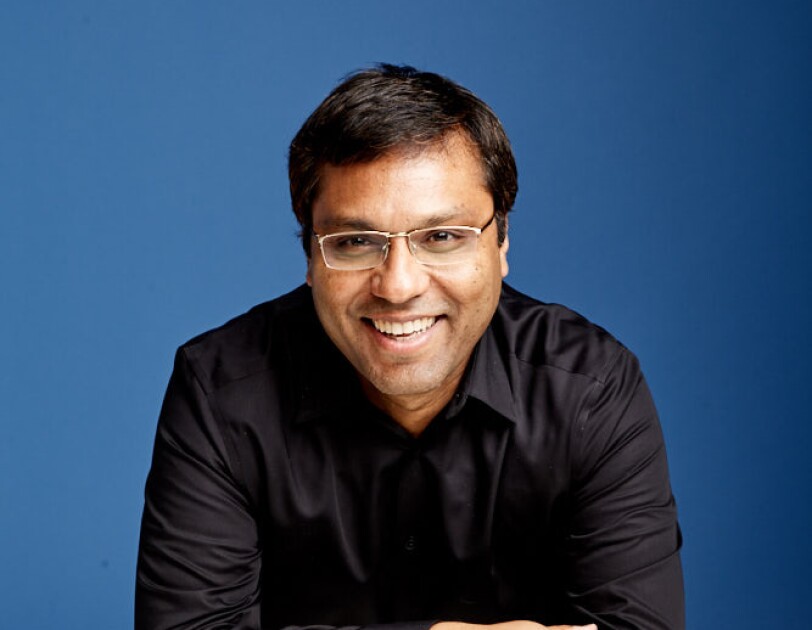 A portrait of Rohit Prasad, vice president and head scientist, Alexa AI. He is wearing a black shirt and is photographed against a blue background.