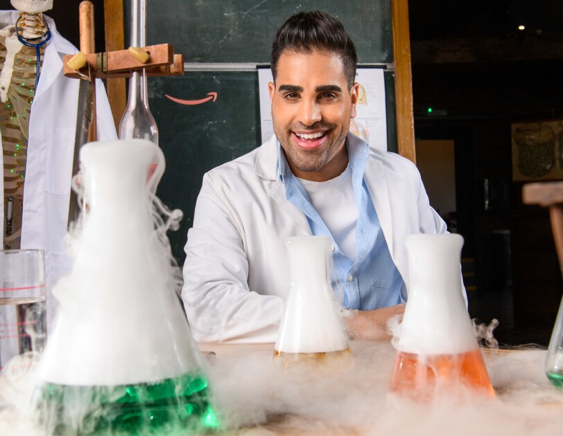 Dr. Ranj Magic Breakfast in front of a table filled with test tubes and science experiments.