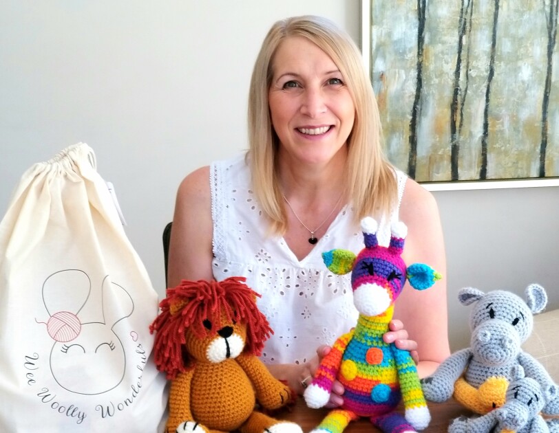 Lisa Dobbs from Wee Woolly Wonderfuls sitting behind some of the toys that she has made using her crochet kits.