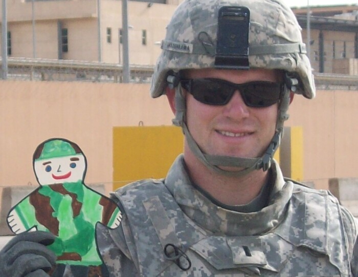 Aaron Guaderrama in combat uniform, holding a child's paper cutout of a soldier in camouflage