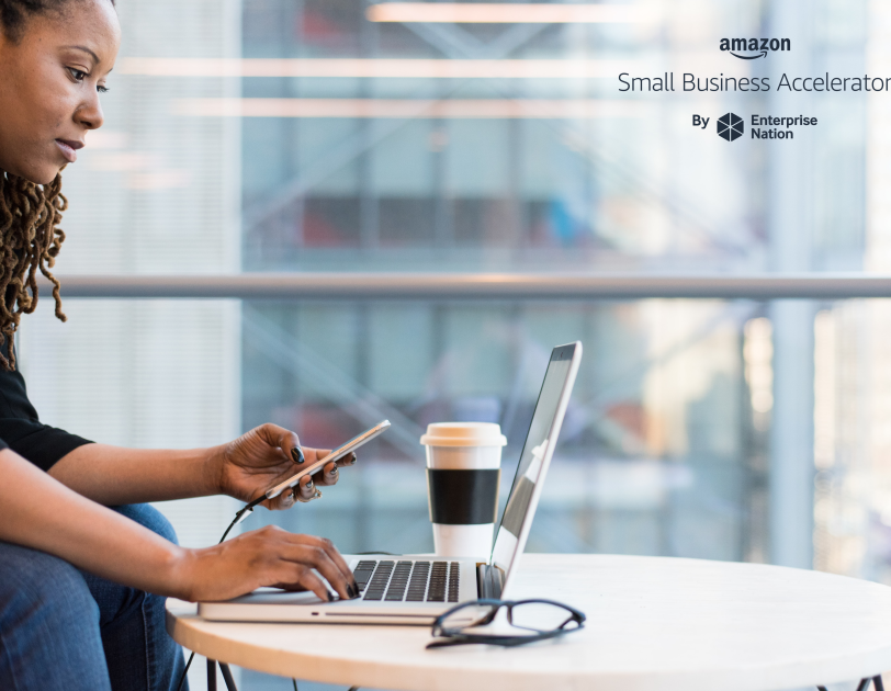 Woman sat typing on a laptop with mobile phone in other hand