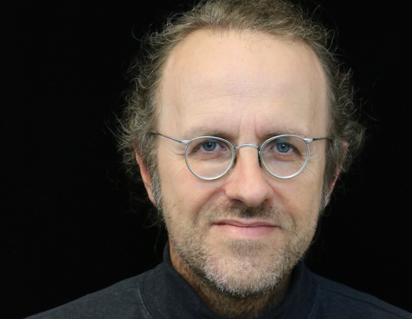 Bernhard Schölkopf, chief machine learning scientist for Amazon’s retail division, he wears a black turtle neck and wire framed silver glasses, and sits in front of a black background.